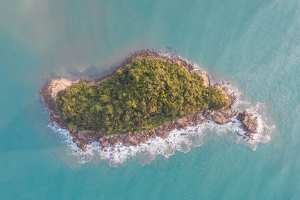 Vista aérea de uma ilha verde cercada por águas azul-turquesa no litoral de Ubatuba, São Paulo.