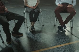 Três adultos sentados em cadeiras participam de uma discussão em um ambiente interno.