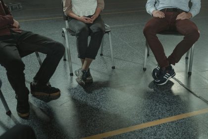 Três adultos sentados em cadeiras participam de uma discussão em um ambiente interno.