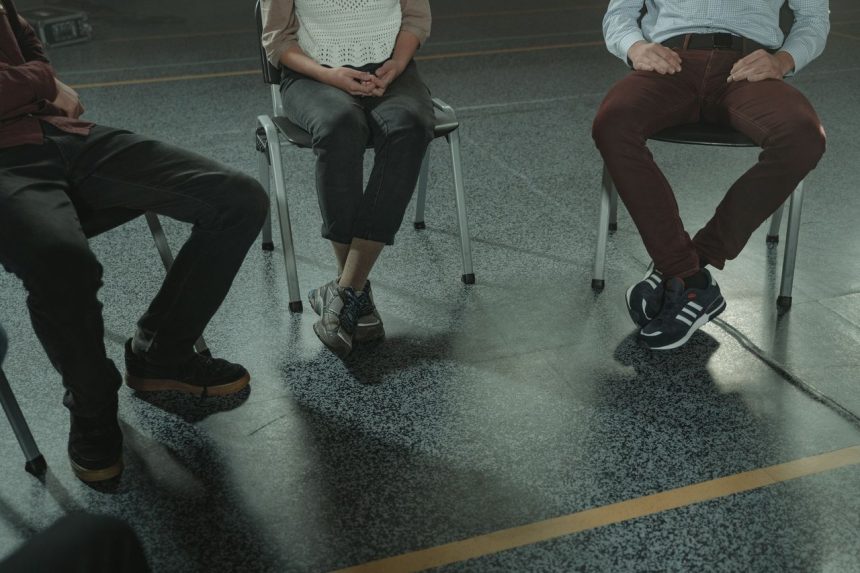 Três adultos sentados em cadeiras participam de uma discussão em um ambiente interno.