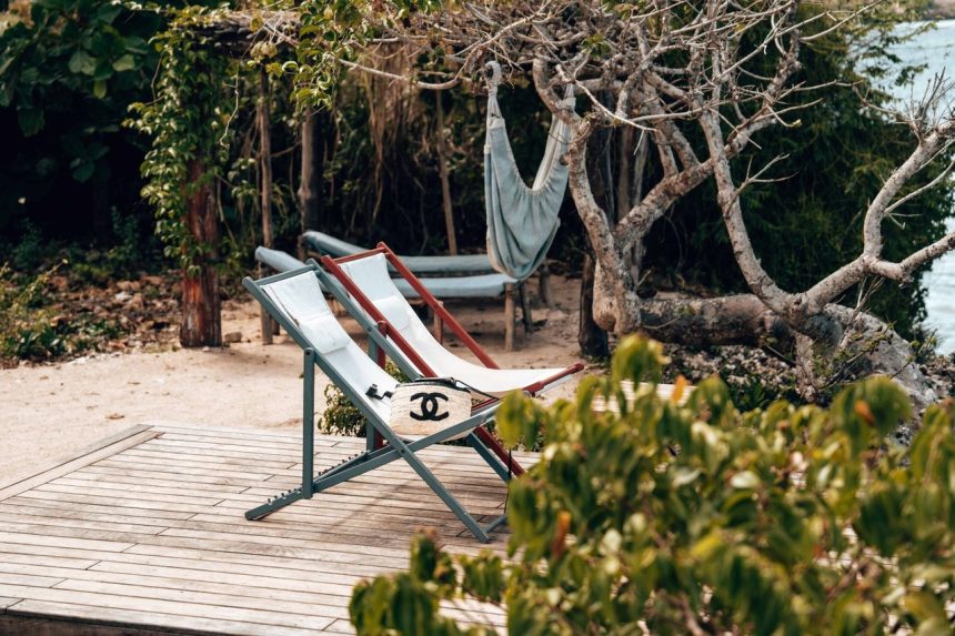 Deck externo com espreguiçadeiras diante do mar, cercado por vegetação.